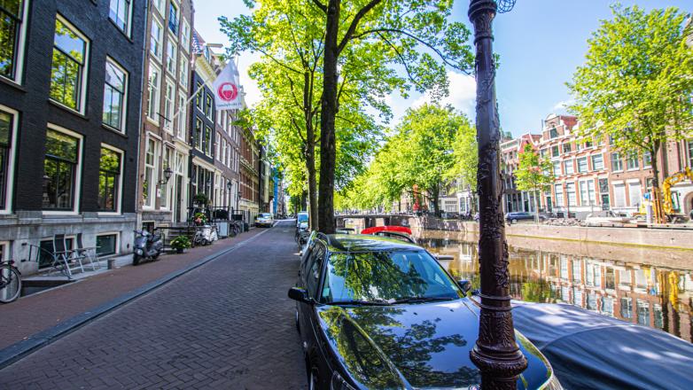 Straat met auto's en grachten langs de Herengracht 221 in Amsterdam
